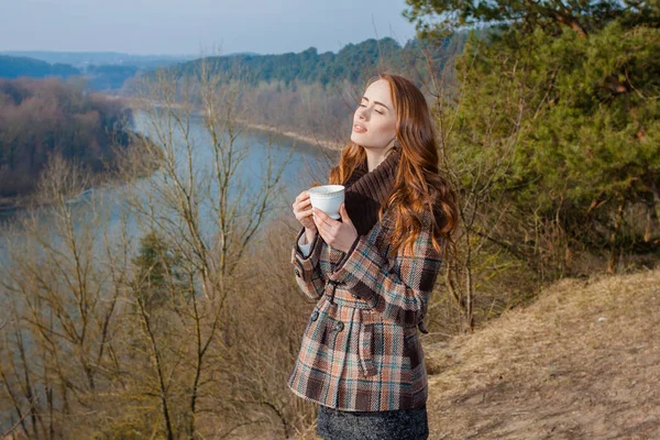 在户外喝一杯的浪漫女孩 嬉皮士姑娘在春天的山水里喝茶 图库图片
