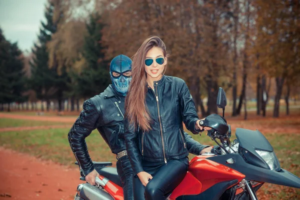 頭蓋骨のマスクの男とスポーツバイクの上の美しいヒップスターの女の子の肖像画 ストック写真