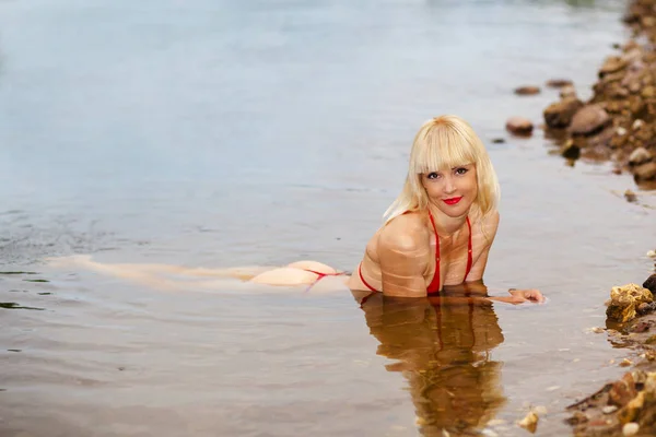 湿惊人的女人在比基尼 穿着比基尼在水里的漂亮女孩 在岸上摆姿势的健身模型 图库照片