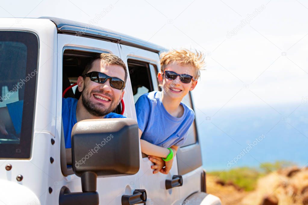 happy positive caucasian boy in sunglasses and his father peeking out of the car window, tropical family vacation or active road trip concept, copy space on right