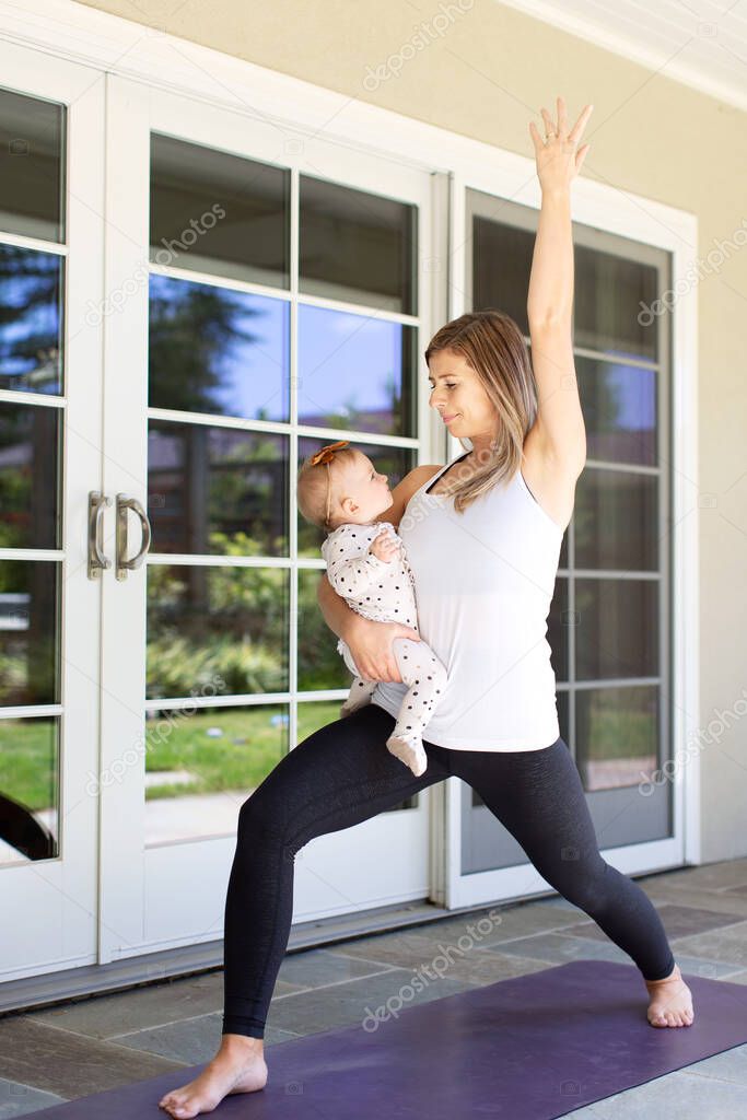 busy young mother doing yoga fitness at home together with her baby during stay-at-home order, healthy family activity concept