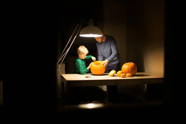 2人家族父と息子ハロウィーンのカボチャを自宅で暗く彫るハロウィーンのコンセプト ストック画像