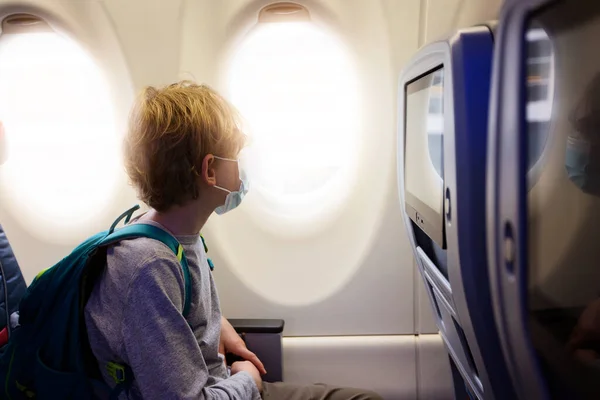 飛行機の客室に座って顔のマスクを身に着けている男の子 コロナウイルスのパンデミックの概念の間に旅行 — ストック写真