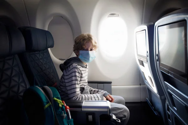 飛行機の客室に座って顔のマスクを身に着けている男の子 コロナウイルスのパンデミックの概念の間に旅行 — ストック写真