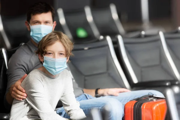 2人家族父と息子空港ターミナルに座って顔のマスクを着てコロナウイルスのパンデミックの概念の間に旅行右側のコピースペース ストック写真