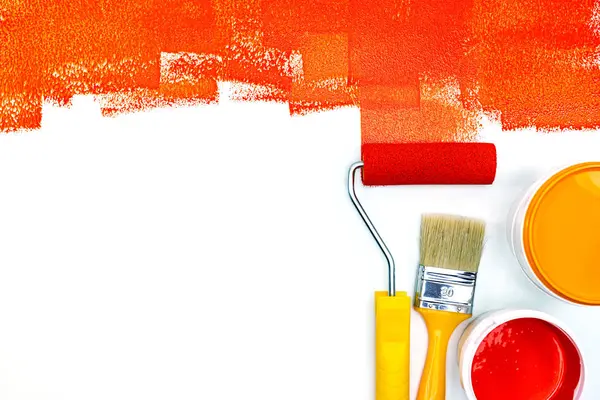 red paint strokes on white desk. red and orange paint can, brush and roller flat view