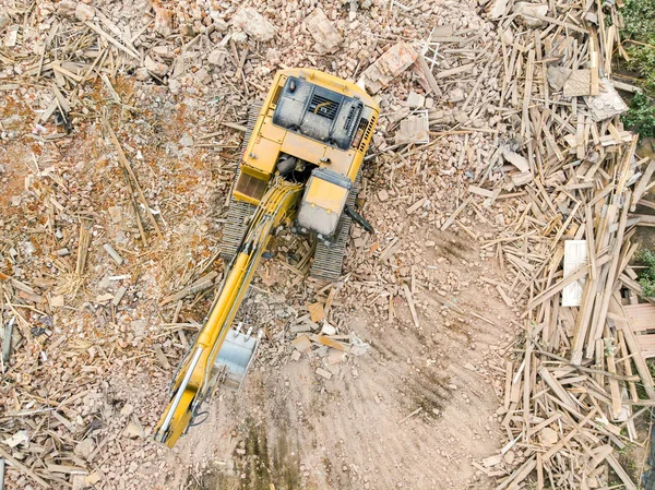 orange tracked excavator on pile of debris of destroyed building. aerial photo