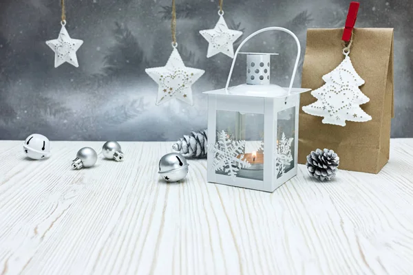 christmas tree decorations with handmade paper present bag and burning candle lantern on grey frosty winter background