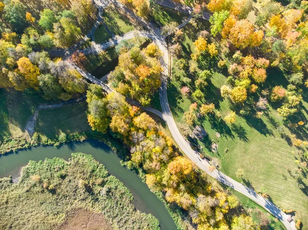 aerial top view of park in autumn. park scene image with yellow trees, asphalt sidewalks and river