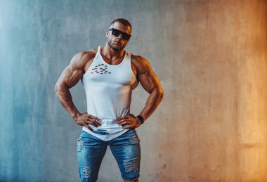 Güçlü delikanlı vücut geliştirmeci taş duvar arka plan üzerinde. Serin ve sıcak ışık efekti.