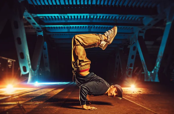 Young cool man break dancer standing on hands upside down. Urban bridge with cool and warm lights background.