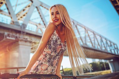 Köprü portre altında duran genç gülümseyen kadın. Sıcak günbatımı ışığı.