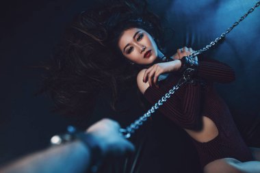 Zincirli seksi bdsm tarzı portresi olan Asyalı genç bir kadın. Erkek el zinciri.