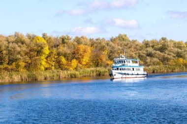 Büyük bir sonbahar nehri boyunca yürüyen küçük beyaz bir vapur.