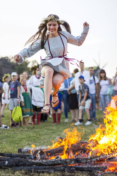 KYIV, UKRAINE - JULY 6, 2018: Young girl jumps over the flames of bonfire during the traditional Slavic celebration of Ivana Kupala holiday in Pirogovo open-air ukrainian folk museum