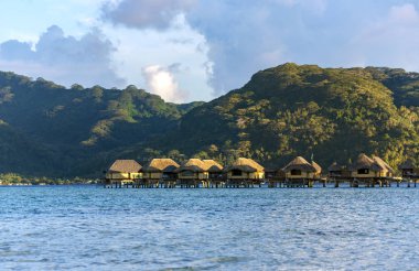 Lüks Klasik thatched çatı bungalow resort Bora Bora, Fransız Polinezyası günbatımı ışınları içinde ahşap bir duba üzerinde.
