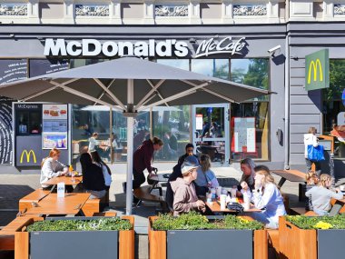 LATVIA, RIGA, SEPTEMBER, 04, 2025: Bir yaz günü insanlar Riga Old Town, Letonya 'da bir McDonalds kafesinin açık verandasında yemek yerler.