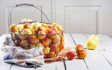 Olgun taze kayısılar ve elmalar dokunmuş metal sepetin içinde odasındaki ahşap masanın üzerinde.