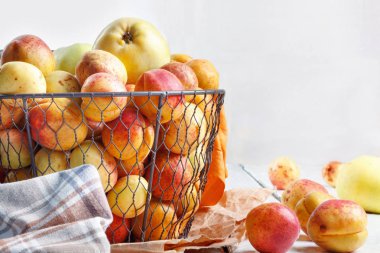 Olgun taze kayısılar ve elmalar dokunmuş metal sepetin içinde odasındaki ahşap masanın üzerinde.