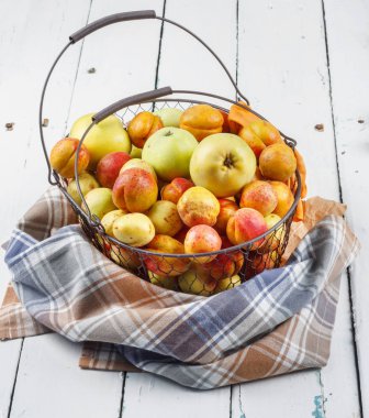 Olgun taze kayısılar ve elmalar dokunmuş metal sepetin içinde odasındaki ahşap masanın üzerinde.