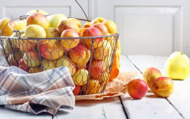 Olgun taze kayısılar ve elmalar dokunmuş metal sepetin içinde odasındaki ahşap masanın üzerinde.