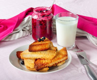 Lezzetli tost ekmeği ev yapımı frenk üzümü reçeli ve parlak kırmızı masa örtüsü üzerinde süt.