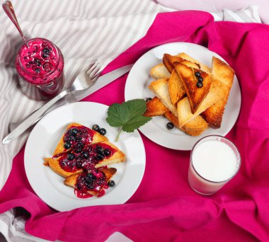 Lezzetli tost ekmeği ev yapımı frenk üzümü reçeli ve parlak kırmızı masa örtüsü üzerinde süt.