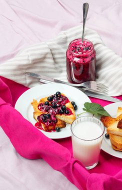 Lezzetli tost ekmeği ev yapımı frenk üzümü reçeli ve parlak kırmızı masa örtüsü üzerinde süt.