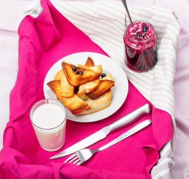 Lezzetli tost ekmeği ev yapımı frenk üzümü reçeli ve parlak kırmızı masa örtüsü üzerinde süt.
