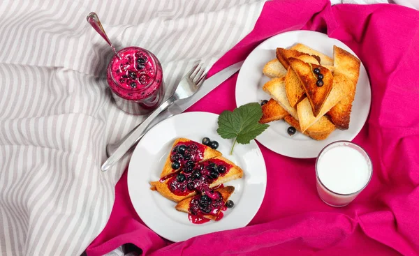 Lezzetli tost ekmeği ev yapımı frenk üzümü reçeli ve parlak kırmızı masa örtüsü üzerinde süt.