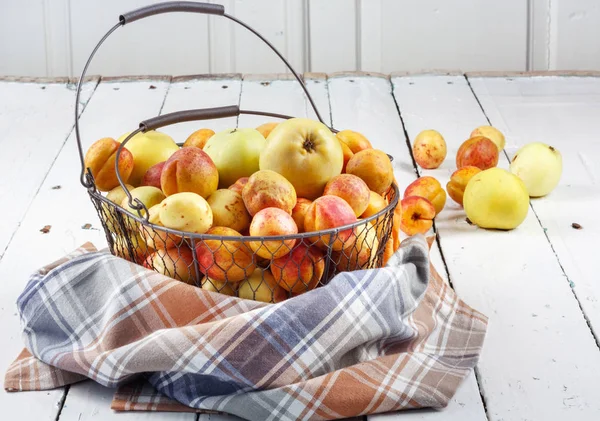 Olgun taze kayısılar ve elmalar dokunmuş metal sepetin içinde odasındaki ahşap masanın üzerinde.