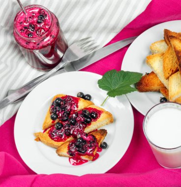 Lezzetli tost ekmeği ev yapımı frenk üzümü reçeli ve parlak kırmızı masa örtüsü üzerinde süt.