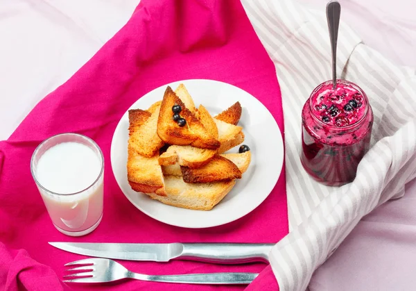 Lezzetli tost ekmeği ev yapımı frenk üzümü reçeli ve parlak kırmızı masa örtüsü üzerinde süt.
