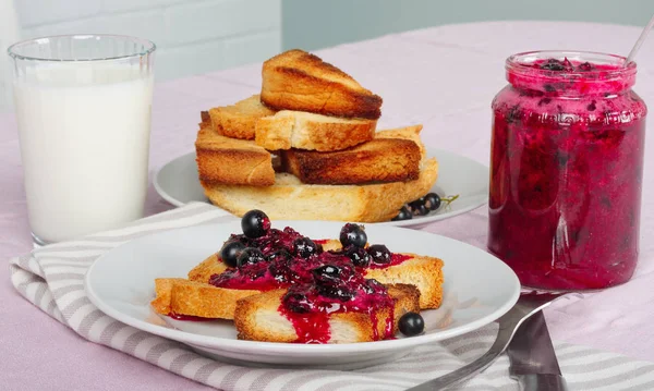 Lezzetli tost ekmeği ev yapımı frenk üzümü reçeli ve parlak kırmızı masa örtüsü üzerinde süt.