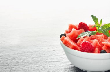 Siyah taş tezgah üzerinde karpuz, ahududu ve Frenk üzümü yeşil nane ile taze sulu adet salata yaprakları