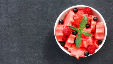 Siyah taş tezgah üzerinde karpuz, ahududu ve Frenk üzümü yeşil nane ile taze sulu adet salata yaprakları
