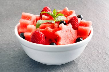 Siyah taş tezgah üzerinde karpuz, ahududu ve Frenk üzümü yeşil nane ile taze sulu adet salata yaprakları