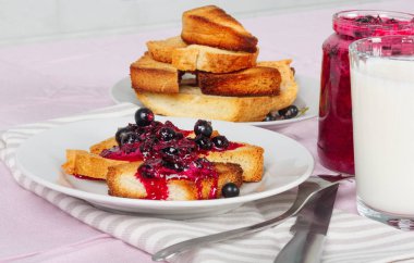 Lezzetli tost ekmeği ev yapımı frenk üzümü reçeli ve parlak kırmızı masa örtüsü üzerinde süt.
