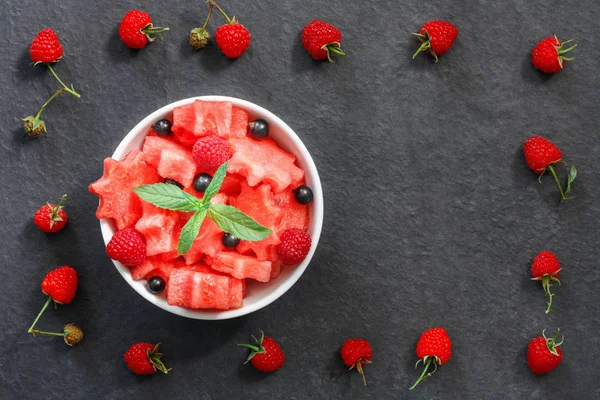 Siyah taş tezgah üzerinde karpuz, ahududu ve Frenk üzümü yeşil nane ile taze sulu adet salata yaprakları