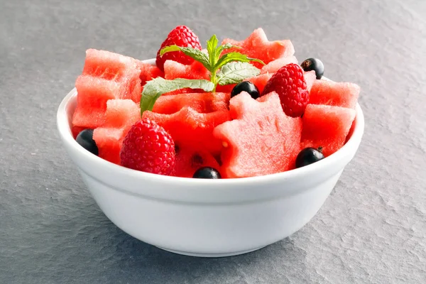 Siyah taş tezgah üzerinde karpuz, ahududu ve Frenk üzümü yeşil nane ile taze sulu adet salata yaprakları