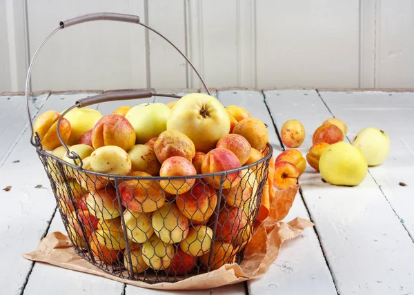 Olgun taze kayısılar ve elmalar dokunmuş metal sepetin içinde odasındaki ahşap masanın üzerinde.