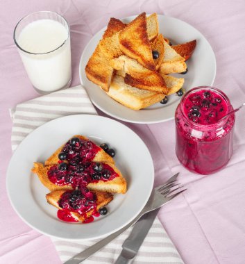 Lezzetli tost ekmeği ev yapımı frenk üzümü reçeli ve parlak kırmızı masa örtüsü üzerinde süt.
