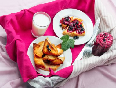 Lezzetli tost ekmeği ev yapımı frenk üzümü reçeli ve parlak kırmızı masa örtüsü üzerinde süt.