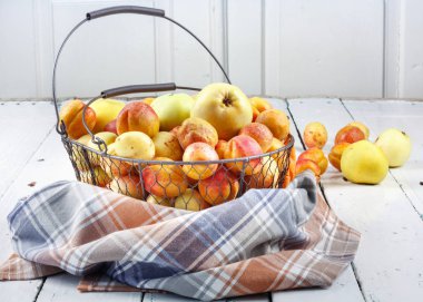 Olgun taze kayısılar ve elmalar dokunmuş metal sepetin içinde odasındaki ahşap masanın üzerinde.