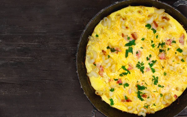 Pastırma, makarna ve Yeşiller eski siyah kızartma tavası vintage ahşap masa arka plan üzerinde tarih ile geleneksel rustik omlet. Kopya girintili