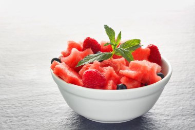 Siyah taş tezgah üzerinde karpuz, ahududu ve Frenk üzümü yeşil nane ile taze sulu adet salata yaprakları