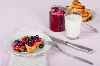 Lezzetli tost ekmeği ev yapımı frenk üzümü reçeli ve parlak kırmızı masa örtüsü üzerinde süt.