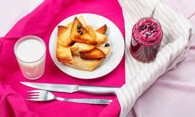 Lezzetli tost ekmeği ev yapımı frenk üzümü reçeli ve parlak kırmızı masa örtüsü üzerinde süt.