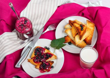 Lezzetli tost ekmeği ev yapımı frenk üzümü reçeli ve parlak kırmızı masa örtüsü üzerinde süt.