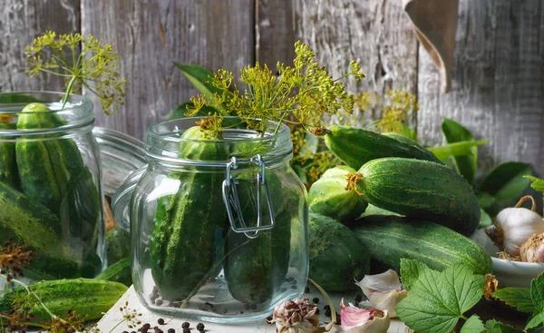 Preserved cucumbers in glass jars with garlic and dill on wooden table